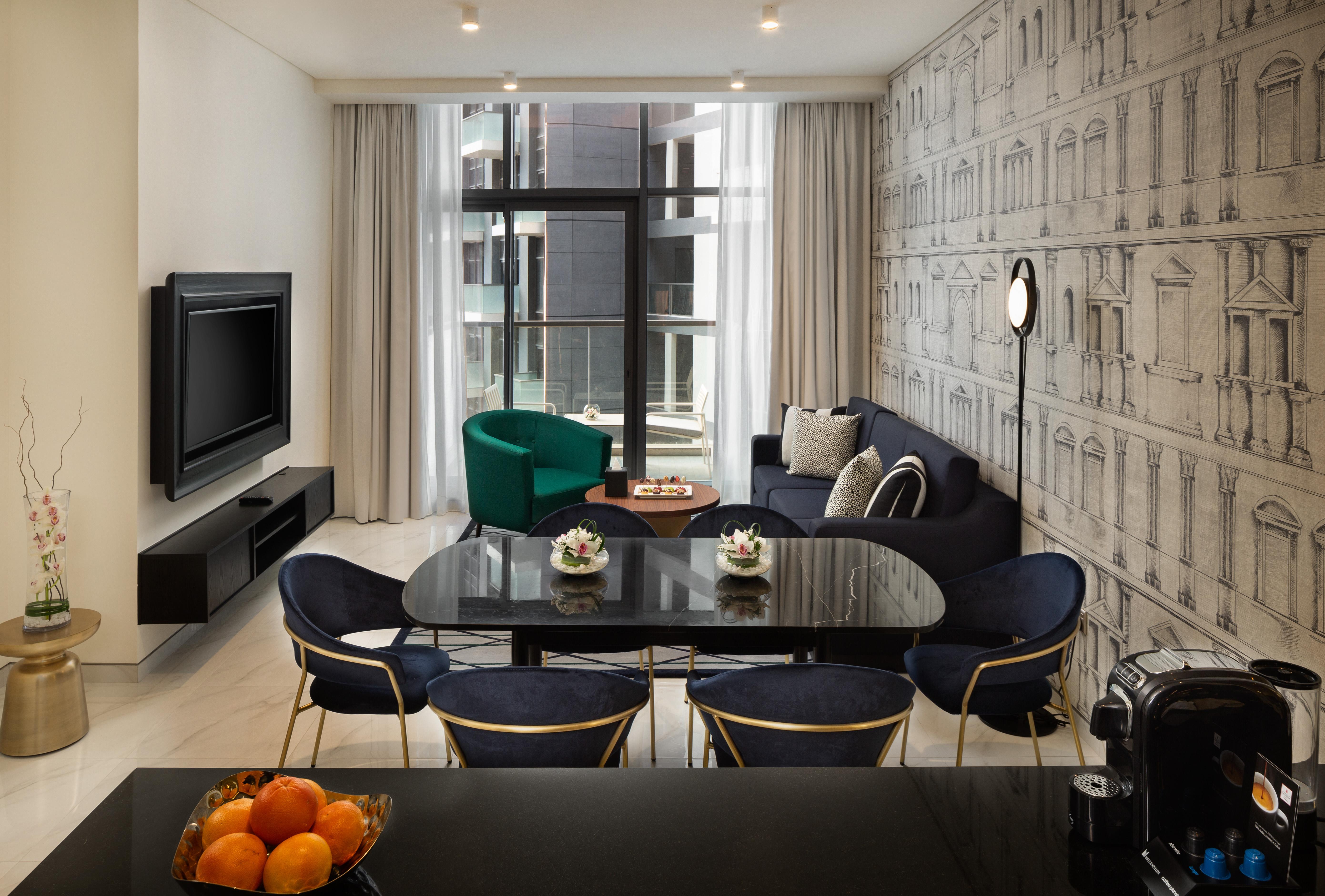 Millennium Atria Business Bay Aparthotel Dubai Luaran gambar The photo shows a modern living space that includes a cozy seating area and dining setup. On the left, there is a large television mounted on the wall. The living room features a blue sofa and a green accent chair, creating a stylish contrast. A smal
