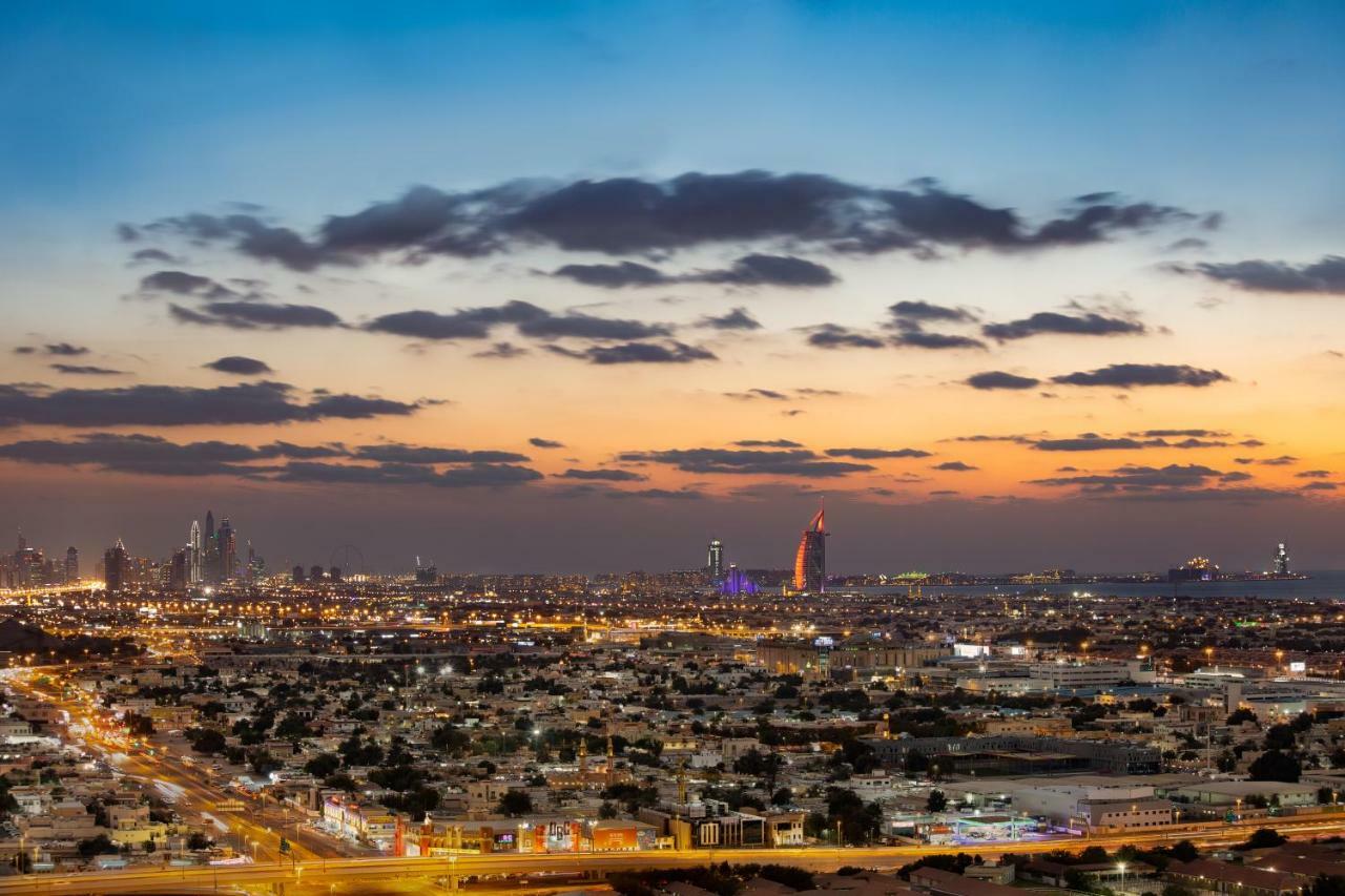 Millennium Atria Business Bay Aparthotel Dubai Luaran gambar The photo shows a stunning cityscape at dusk, with a panoramic view of a city skyline. The sky is transitioning from blue to orange, indicating sunset, with scattered clouds creating a colorful backdrop. In the foreground, you can see a sprawling urb