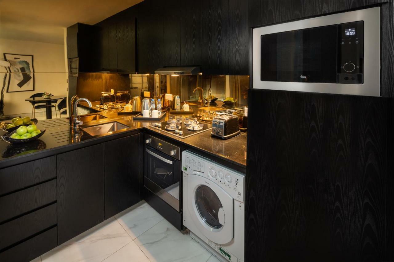 Millennium Atria Business Bay Aparthotel Dubai Luaran gambar The photo shows a modern kitchen with a sleek design. The cabinets and surfaces are predominantly black, creating a contemporary look. There is a stainless steel microwave mounted above the countertop, and on the counter, various kitchen appliances l