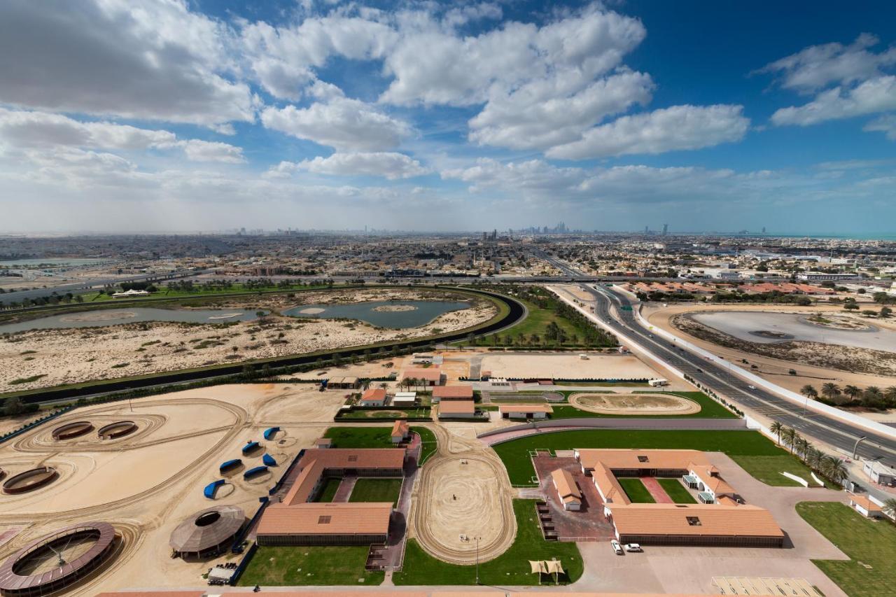 Millennium Atria Business Bay Aparthotel Dubai Luaran gambar The photo shows a panoramic view of a large landscape with expansive open areas, buildings, and a curved track. In the foreground, there are several stable structures and facilities associated with horse training or racing, surrounded by well-maintai